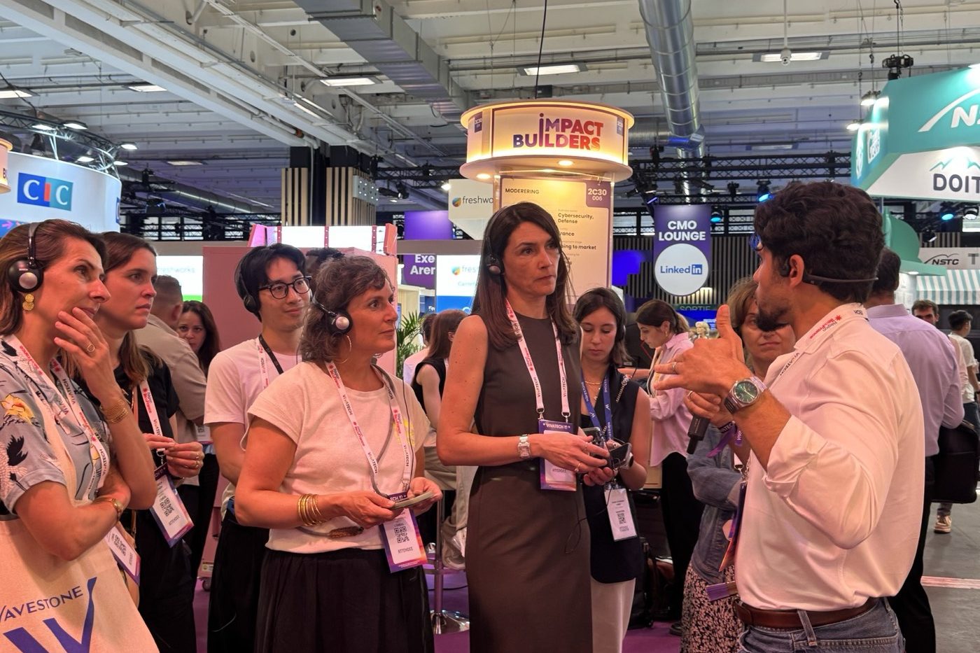 Visitors talking at a conference booth, some wearing headphones